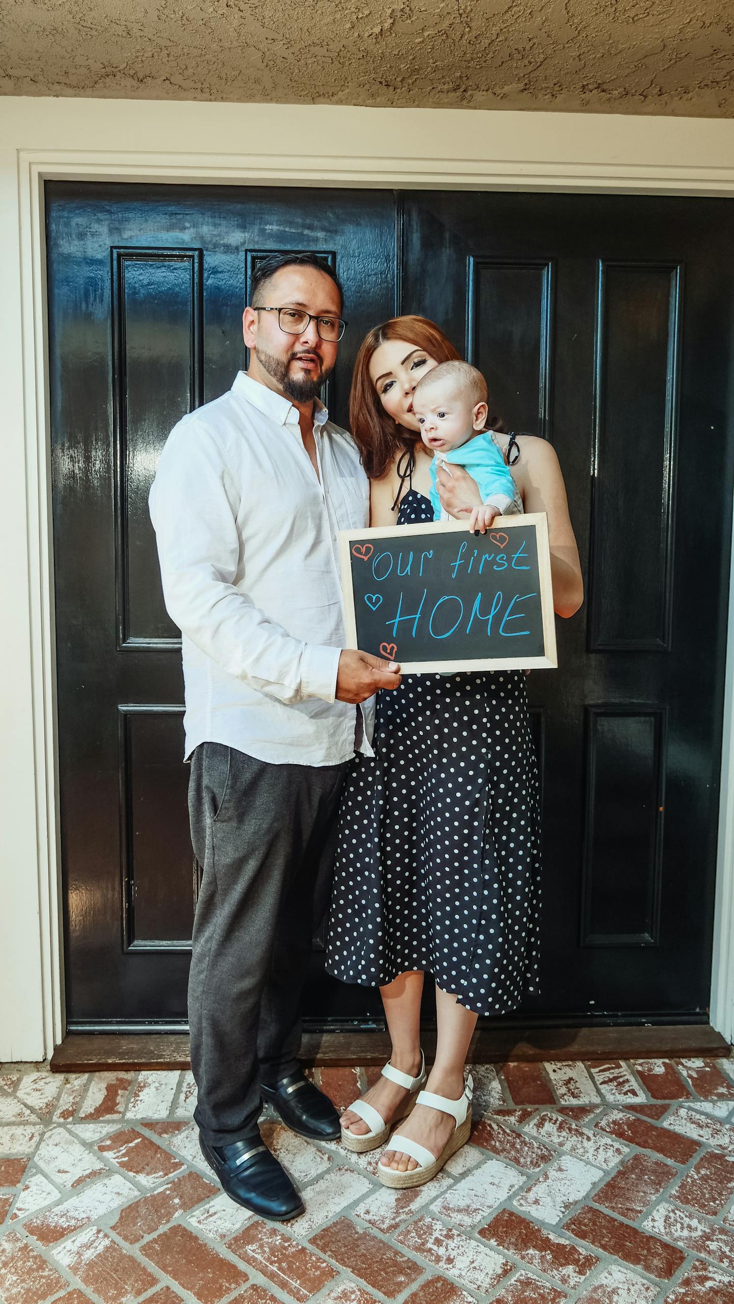 A couple with a baby joyfully holding a sign for their new home.